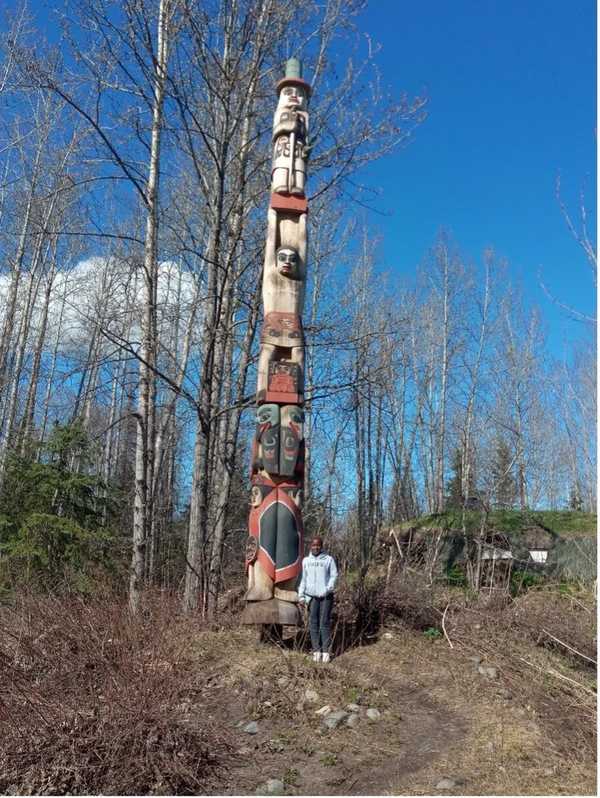 An African woman stands by a totem pole