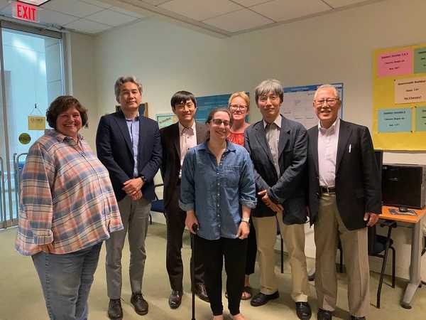 Seven people of various genders, races, and abilities standing in a classroom and posing for the photo, smiling.